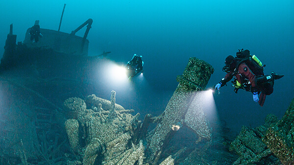 3 divers shine their light on a shipwreck