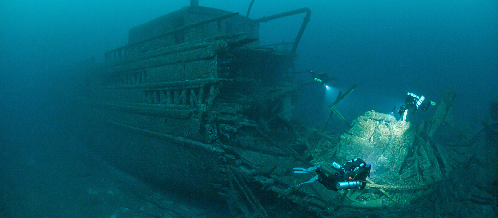 3 Divers shine lights on a shipwreck