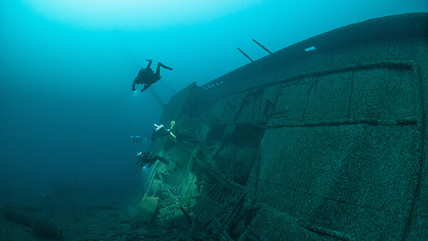 3 divers swim near a shipwreck resting on its side
