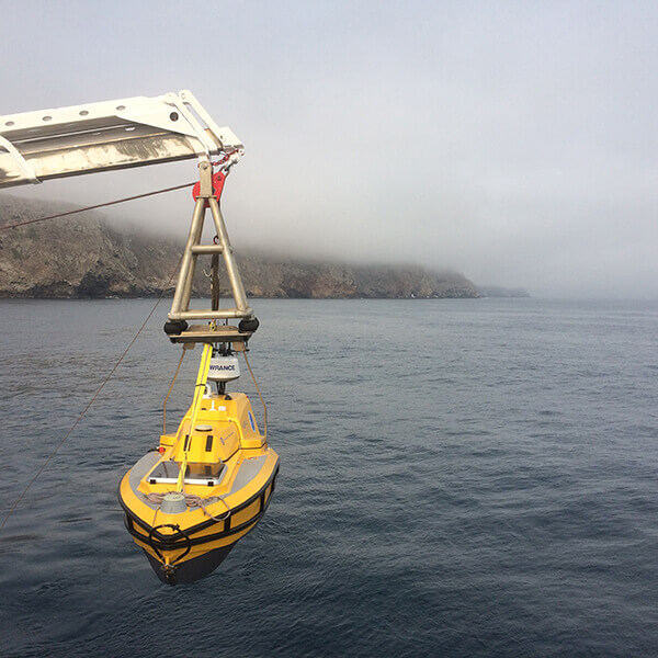 A yellow rov suspended over water by a crane
