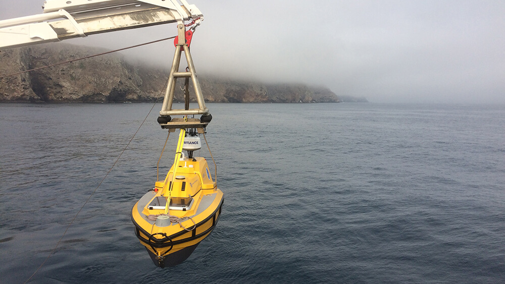 A yellow rov extended above water by a crane
