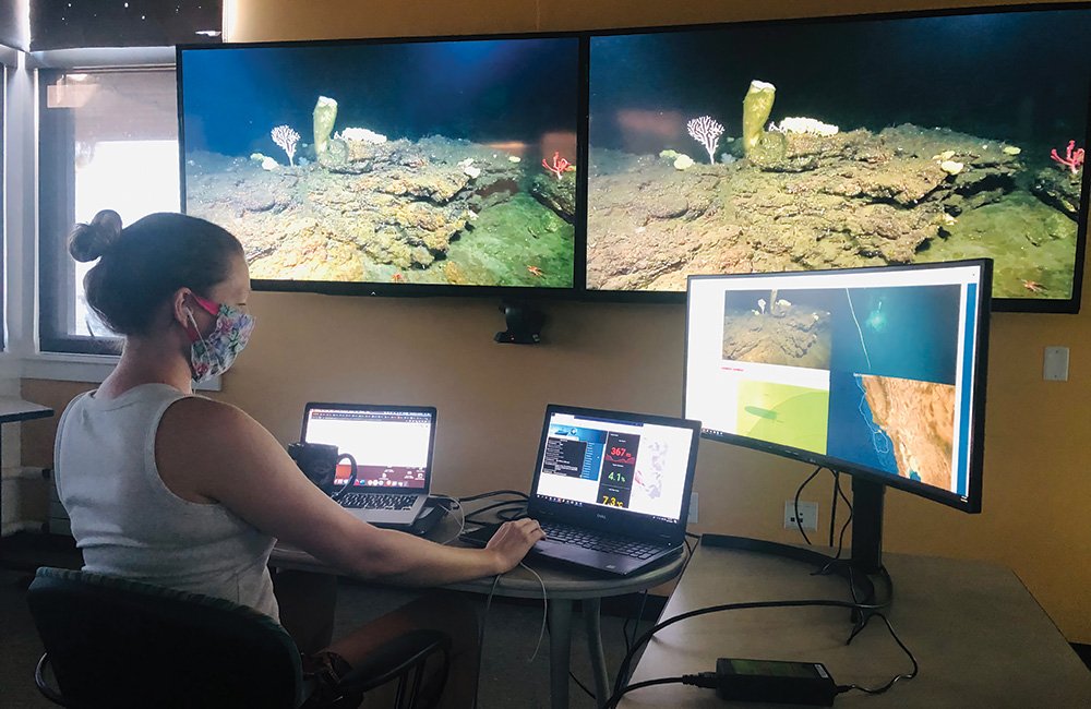 women working on a computer while a live stream from an rov runs in the background