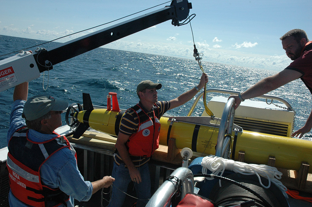 three researchers stand on the deck of a ship about to launch an AUV