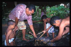 photo of man and two boy tending an underground oven