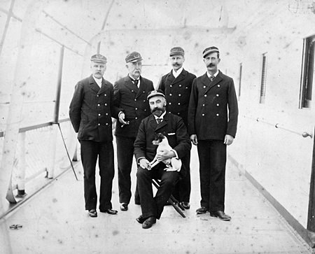 photo of five officers on board the SS City of Rio de Janeiro, Joseph Matthews, Chief Engineer, O. K. Freeman, Purser, Harry Kirulff, Surgeon, Caterinich, First Officer, center with dog, J. Tremain Smith, Captain
